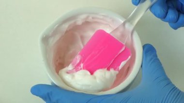 Mavi eldivenli eldivenli ellerin porselen havan ve tokmak kullanarak krem karıştırdığı kozmetik laboratuvar sürecinin makro görüntüsü.. 