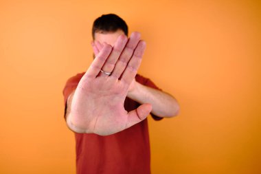 Kırmızı tişört ve kot pantolonla turuncu bir duvarın yanında poz veren erkek model. El hareketleri ve duygular. Stüdyo fotoğrafçılığı. Duygu, güç ve eğlence kavramı. Günlük kıyafet.