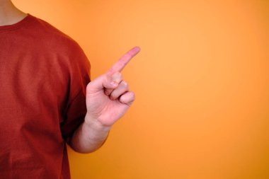 Kırmızı tişört ve kot pantolonla turuncu bir duvarın yanında poz veren erkek model. El hareketleri ve duygular. Stüdyo fotoğrafçılığı. Duygu, güç ve eğlence kavramı. Günlük kıyafet.