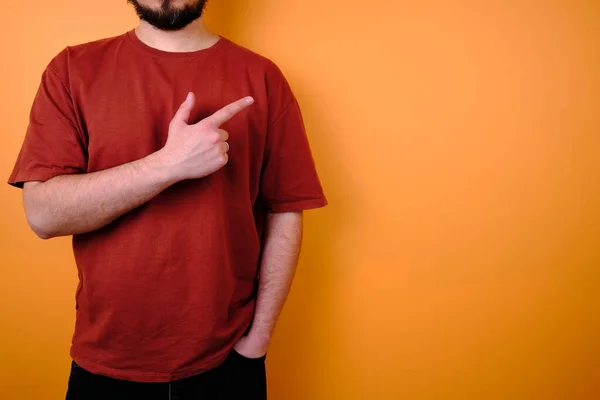 stock image Male model posing near an orange wall in a red T-shirt and jeans. Hand gestures and emotions. Studio photography. The concept of emotion, strength and fun. Casual wear