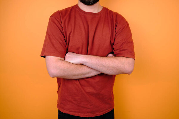 Male model posing near an orange wall in a red T-shirt and jeans. Hand gestures and emotions. Studio photography. The concept of emotion, strength and fun. Casual wear