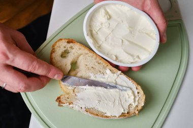 Adam bir parça taze ekmeği bıçakla keser ve mutfakta lezzetli bir peynirli sandviç yapar.