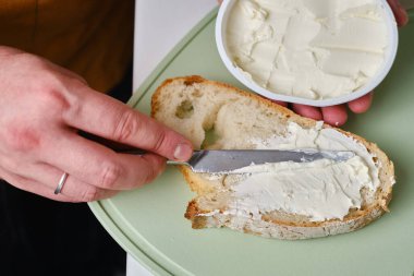 Adam bir parça taze ekmeği bıçakla keser ve mutfakta lezzetli bir peynirli sandviç yapar.