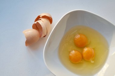 Beyaz arka planda çiğ yumurta ve yumurta kabuğu kasesi. Yumurta sağlıklı bir yemektir.