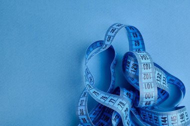 Mavi arka planda mavi bir mezura. Uzunluk ve hacim ölçme aracı. Giysi endüstrisinde veya insan vücudunun hacmini ölçmek için bant