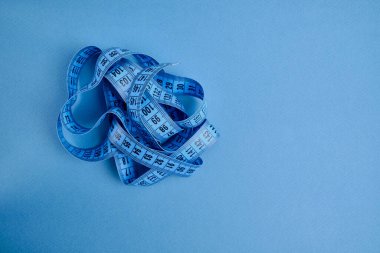 Mavi arka planda mavi bir mezura. Uzunluk ve hacim ölçme aracı. Giysi endüstrisinde veya insan vücudunun hacmini ölçmek için bant