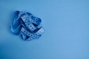Mavi arka planda mavi bir mezura. Uzunluk ve hacim ölçme aracı. Giysi endüstrisinde veya insan vücudunun hacmini ölçmek için bant
