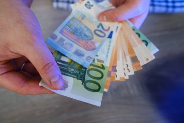 Adam parayı elinde tutuyor. Ödeme ya da takas için euro olarak nakit. Erkek, euro banknotlarında maaşı sayar. Para biriktirmek, banka depozitosu çekmek. Avrupa parası. Finansal kriz. Eller yakın plan.