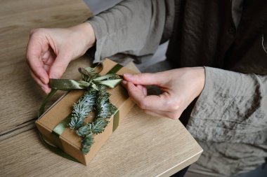 Woman holds a Christmas present in hands. Happy holiday, gift box close-up. Surprise for Boxing day, Christmas and New Year party. Celebration winter event. Wrapping paper, spruce branch and ribbon