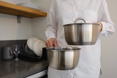 Bir kadın mutfakta elinde metal bir tava tutuyor. Tabaklar yakın plan. Şefin çalışma aletleri.