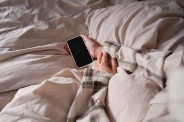 Yatakta akıllı telefonu tutan bir elin yakın çekimi. Kız alarmı kapatmak ya da bir mesaj okumak için cep telefonuna uzandı. Adam elinde bir telefonla uyuyakaldı.