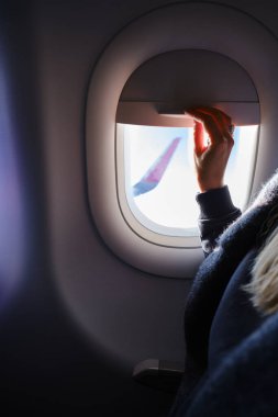 Kadın, uçağın penceresinden telefonla fotoğraf çekiyor. Elinde telefon, lombozun yanında. Uçak kanadı, manzara manzarası. Güzel bulut, mavi gökyüzü. Uçakla seyahat, macera. Hava Taşımacılığı