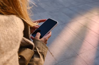 Woman is holding a modern smartphone, sending a text message or using an app on her mobile phone. Internet technology user. Smartphone close-up. Focus on the phone screen