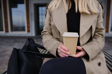 Kadın elinin içinde kahve olan kağıt bardak. Şehirde kahve içme zamanı. Paket kahve. Anın tadını çıkar, mola ver. Tek kullanımlık kağıt bardak yakın plan. Lezzetli sıcak içecek. Metin ve maket için boşluk alanı