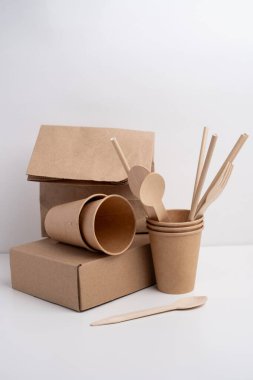 Çevre dostu tek kullanımlık sofra takımı yığını. Tahta çatallar, bıçaklar, kağıt bardaklar ve hafif arka planda tabaklar. Biyo-çözünebilir çatal bıçak takımı ve piknik için tabak, hazır yemek..