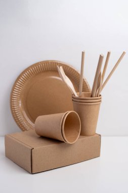 Çevre dostu tek kullanımlık sofra takımı yığını. Tahta çatallar, bıçaklar, kağıt bardaklar ve hafif arka planda tabaklar. Biyo-çözünebilir çatal bıçak takımı ve piknik için tabak, hazır yemek..