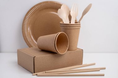 Çevre dostu tek kullanımlık sofra takımı yığını. Tahta çatallar, bıçaklar, kağıt bardaklar ve hafif arka planda tabaklar. Biyo-çözünebilir çatal bıçak takımı ve piknik için tabak, hazır yemek..