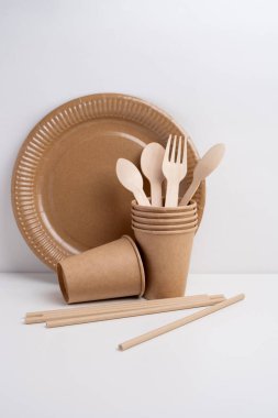 Çevre dostu tek kullanımlık sofra takımı yığını. Tahta çatallar, bıçaklar, kağıt bardaklar ve hafif arka planda tabaklar. Biyo-çözünebilir çatal bıçak takımı ve piknik için tabak, hazır yemek..