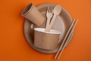 Çevre dostu tek kullanımlık sofra takımı yığını. Tahta çatallar, bıçaklar, kağıt bardaklar ve hafif arka planda tabaklar. Biyo-çözünebilir çatal bıçak takımı ve piknik için tabak, hazır yemek..