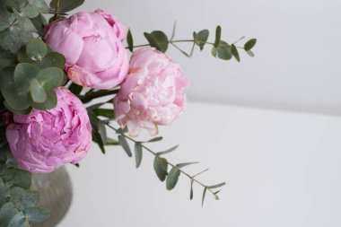 Güzel pembe şakayıklar ve okaliptüs dalları beyaz masa üzerinde metin, üst görünüm ve düz yatış tarzı için yer var.