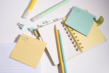 Not defteri, ataçlar, ataçlar ve yapışkan notlar, renkli arka planda kalemler. Ofis ya da okul malzemeleri.