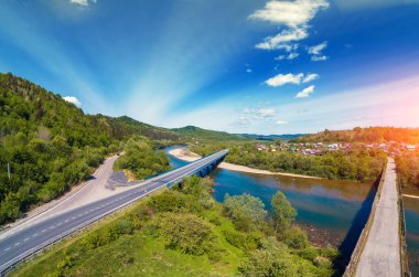 Panoramic aerial view of the mountains valley with village, river and two road bridges
