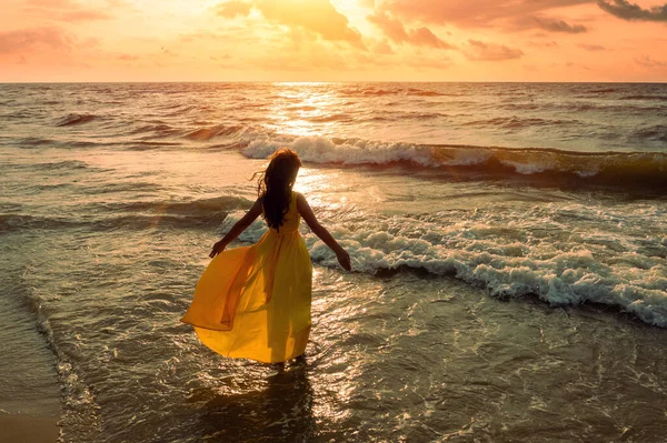 金色日出时的海景 天空美丽 海滩上的女人身穿黄色飘扬衣服的年轻而快乐的女人沿着海滨散步 女孩看着神奇的日出 从上面看 — 图库照片