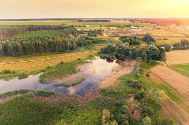Yazın yanan gökyüzü ile kırsalda güzel bir günbatımı. Akşamları kırsal alan. Derenin, köyün ve tarıma elverişli alanların havadan görüntüsü. Panoramik görünüm