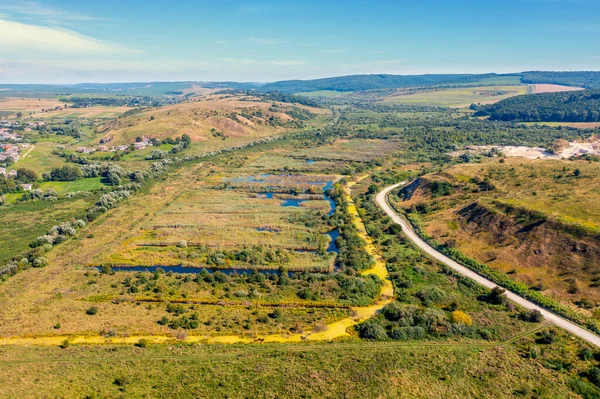 Tepeler arasındaki su basmış çayır manzarası. Tepenin eteğindeki toprak yol. Yaz kırsal arazisi