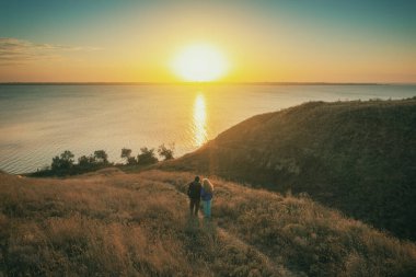 Bir sonbahar akşamında deniz manzarası. Genç çift akşamları bir tepede durur ve güzel bir gün batımını seyrederler.