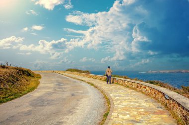 Bir adam güneşli bir günde deniz kenarında gezinti güvertesi yolu boyunca yürür (Estrada do faro)