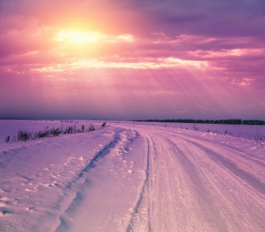Gün batımında kış manzarası. Tarlada karla kaplı bir yol ve akşam güzel bir gökyüzü.