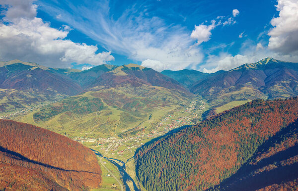 Aerial view of the mountain valley with the river and the small town of Kolochava on a sunny day. Mountain view in autumn. Beautiful natural landscape. Carpathian mountains. Ukraine