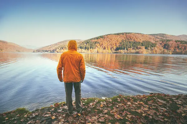 Sonbaharda bir adam bir dağ gölünün kıyısında duruyor.