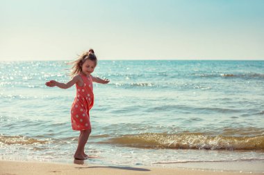 Yazın sahilde yürüyen mutlu küçük kız. Puantiyeli pembe elbiseli bebek.