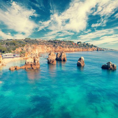 Bulutlu gökyüzü ile deniz manzarası. Kaya sahili. Arrifes Plajı (Praia dos Arrifes), Albufeira, Portekiz.