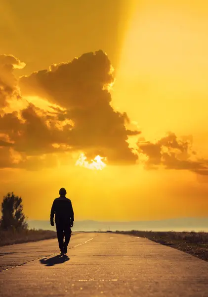 若い男がコンクリートの道を歩き 美しい黄金の日没を見ています 垂直画像について ロイヤリティフリーのストック写真