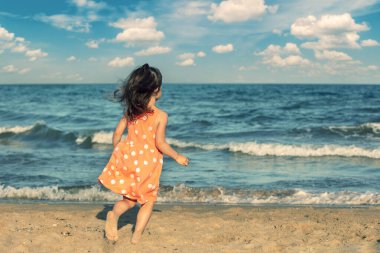 Mutlu küçük kız yazın kumsalda koşar ve kameraya geri döner.
