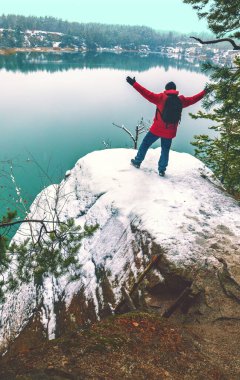 Elleri havada bir adam kışın karlı bir gölün kıyısında durur ve güzel manzaraya bakar. Dikey resim