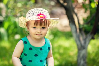 Hasır şapkalı mutlu bebek yaz bahçesinde oturuyor.