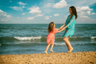 Küçük kızı olan genç, mutlu bir kadın sahilde el ele dans ediyor. Anneler Günü konsepti