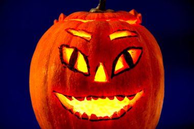 İçinde mum ışığı olan Cadılar Bayramı kabağı koyu mavi bir arka planda