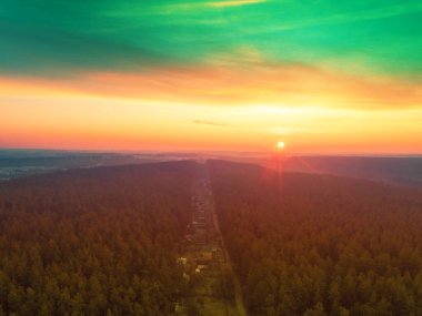 Çam ormanının üzerinde güzel dramatik bir akşam göğü. Gün batımında ormanda bir köy. Hava görünümü