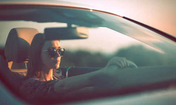 日没時にコンバーチブルの車輪の後ろに眼鏡をかけて若い女性 ロイヤリティフリーのストック画像