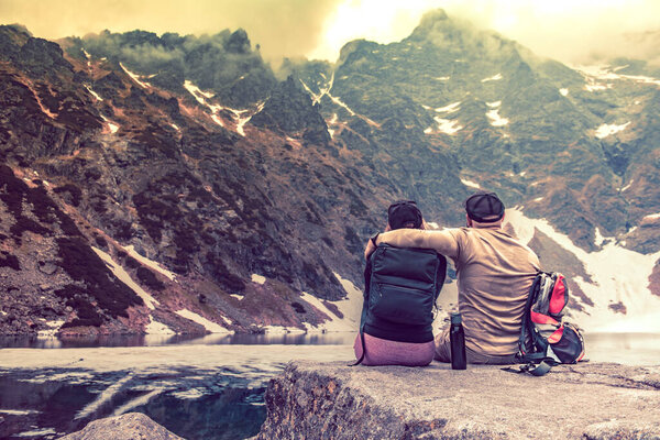 Hugging couple by a mountain lake in the mountains. Cloudy weather. Trekking theme. Cloudy weather.