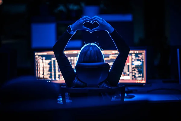 Sign of love shown with hands during night work in the office. Love to work at night. Night work. Working late. Computer screens.