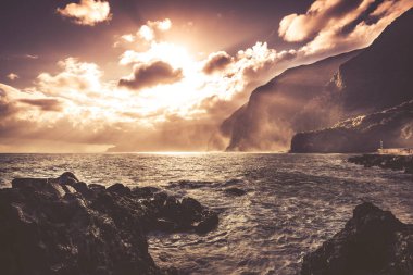 Madeira sahili manzarası. Güneş bulutların arasından doğuyor. Sıcak renkli fotoğraf.