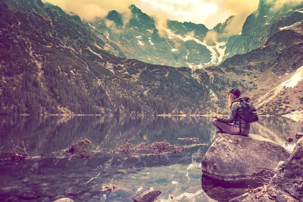 Yoga in the mountains. Searching for peace. Woman sitting on a stone in front of a mountain lake.