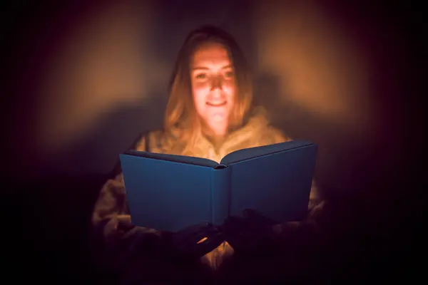 Light from the book. Happy woman reading a book in bed.