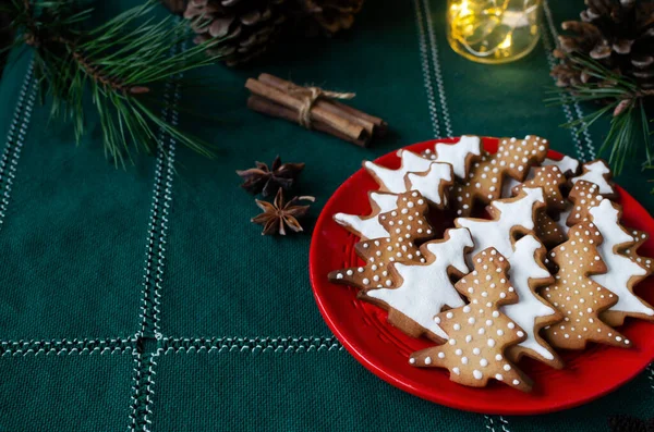ライトのある緑の背景に赤いプレートの上に白いアイシングで飾られたお祭りのクッキー 自家製ジンジャーとシナモンのクリスマスクッキー 水平方向 選択的フォーカス スペースのコピー — ストック写真